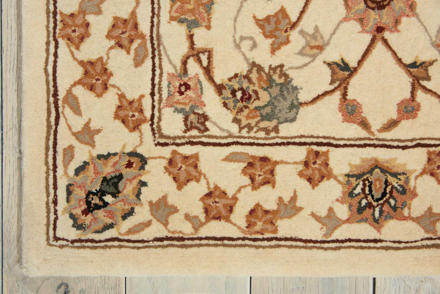 Cream oriental-style rug with brown border and multicolor floral vines on a wooden floor.