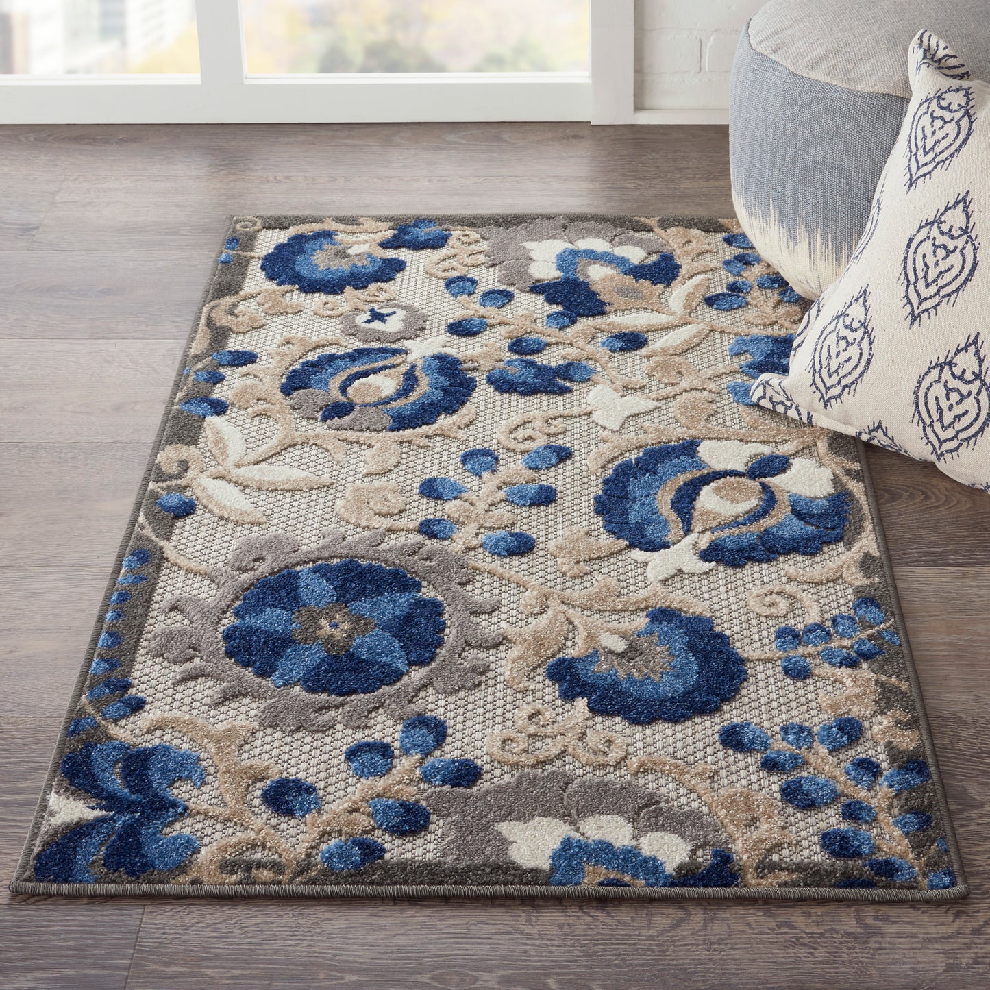 Blue and beige floral area rug on dark wood floor, beside a gray sofa with a patterned pillow.