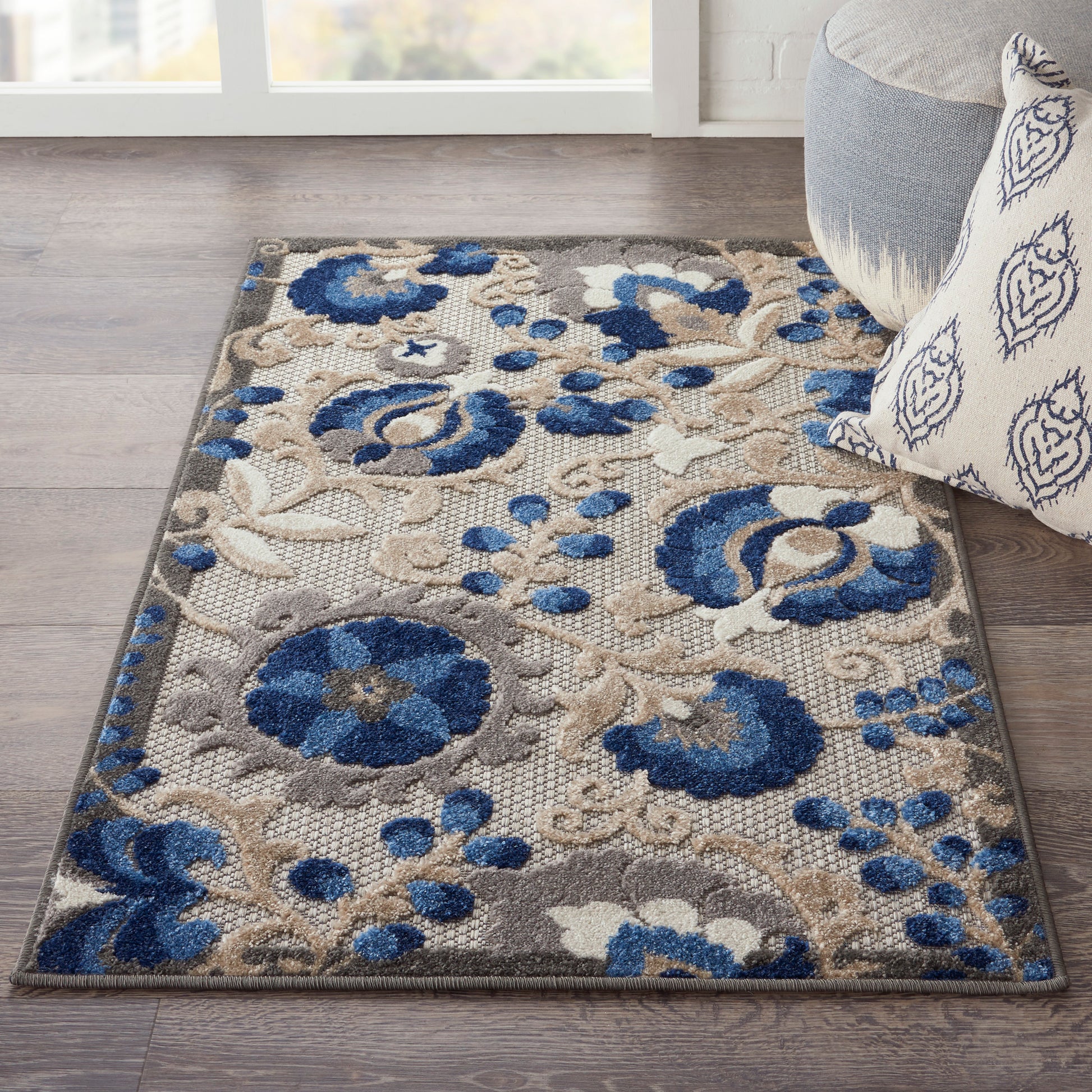 Blue and beige floral area rug on dark wood floor, beside a gray sofa with a patterned pillow.