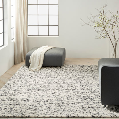 Modern minimalist living room with dark gray ottomans and a speckled black-and-white area rug on light wood floors.