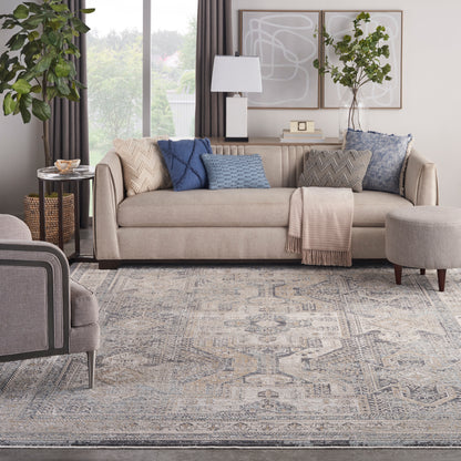 8' x 10' blue-gray area rug in a modern living room with a beige fabric sofa, blue and gray cushions, a throw blanket, and abstract art on the wall.
