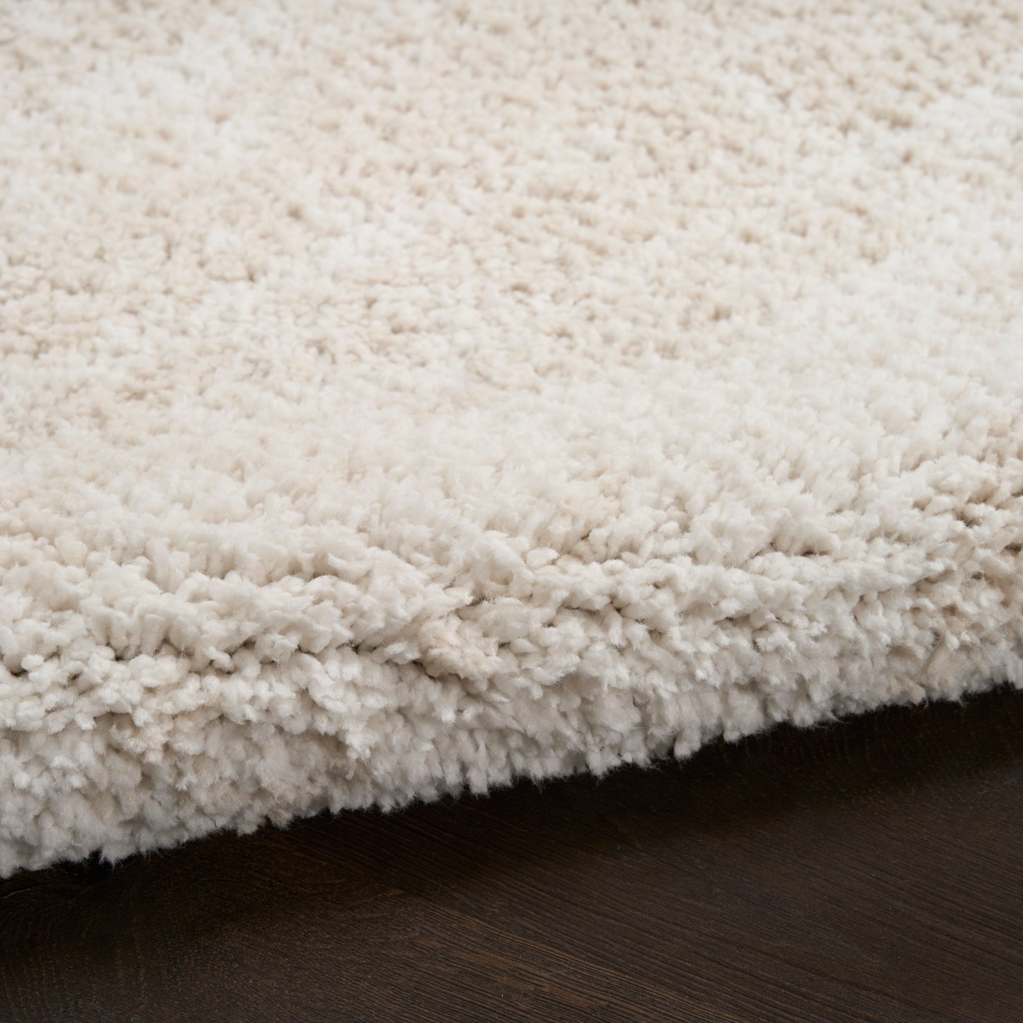Ivory shag rug with dense plush pile and curled fibers on dark wood floor.