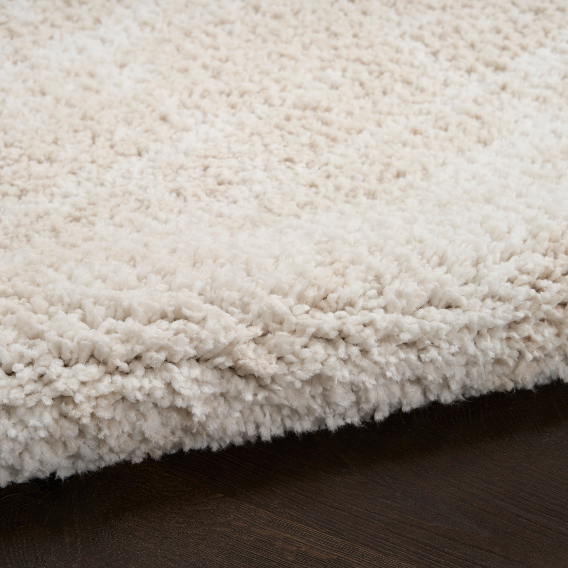 Ivory shag rug with dense plush pile and curled fibers on dark wood floor.