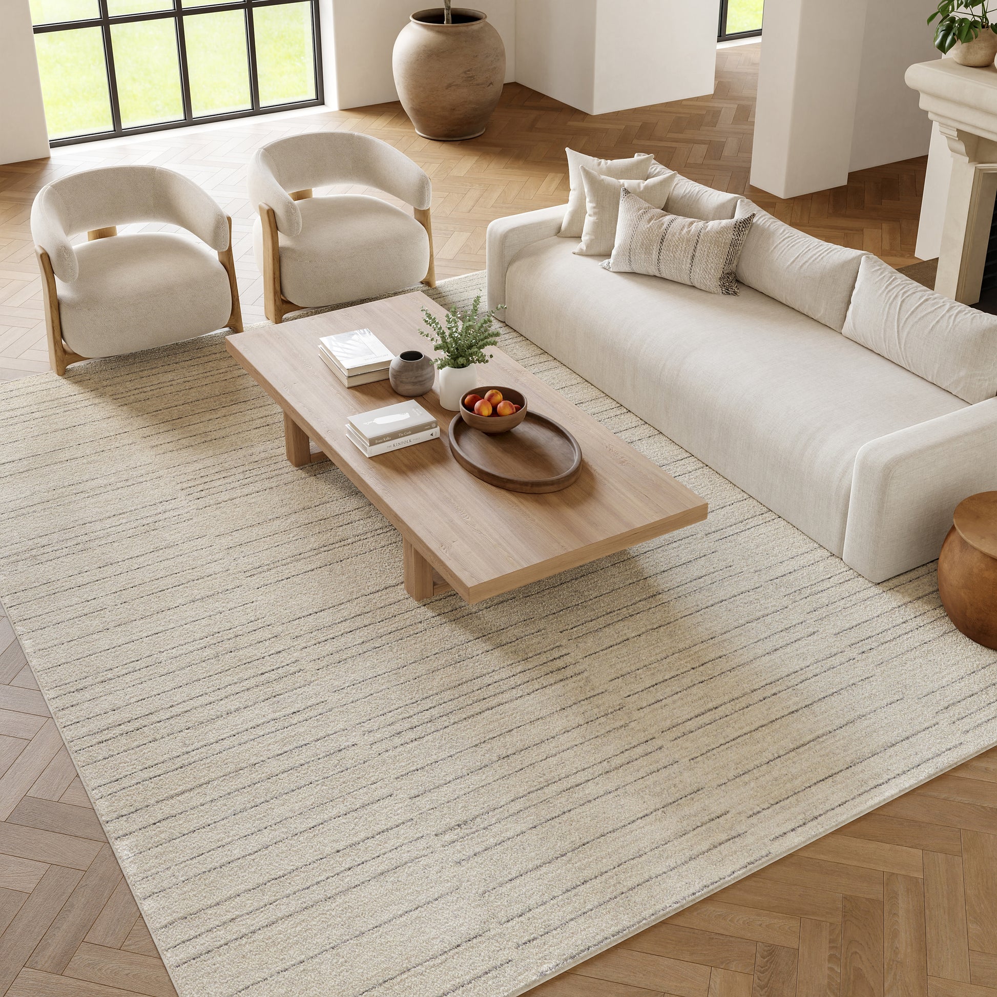 Neutral beige living room with a cream sofa, two curved armchairs, and a wooden coffee table on a striped beige rug.