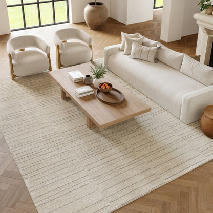 Neutral beige living room with a cream sofa, two curved armchairs, and a wooden coffee table on a striped beige rug.