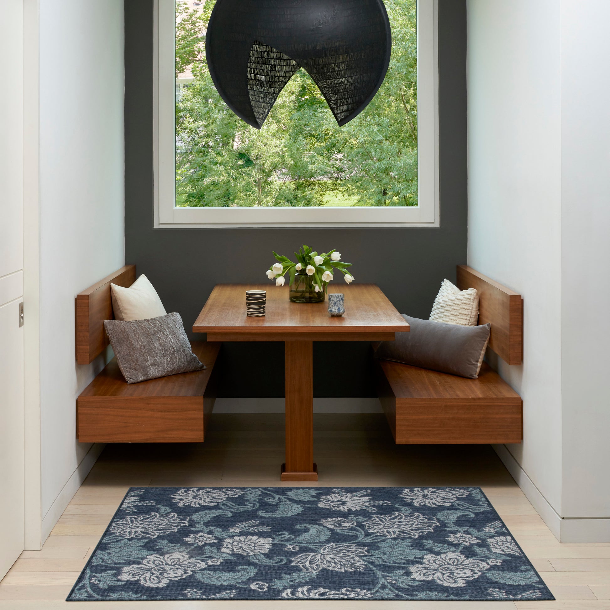 Tropical 3' x 5' rug in a dining nook with built-in benches; blue rug on the floor, a vase of white flowers, and a black pendant light.