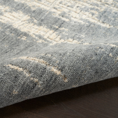 Close-up of a plush gray rug with cream abstract pattern & curled edge on dark wood floor.