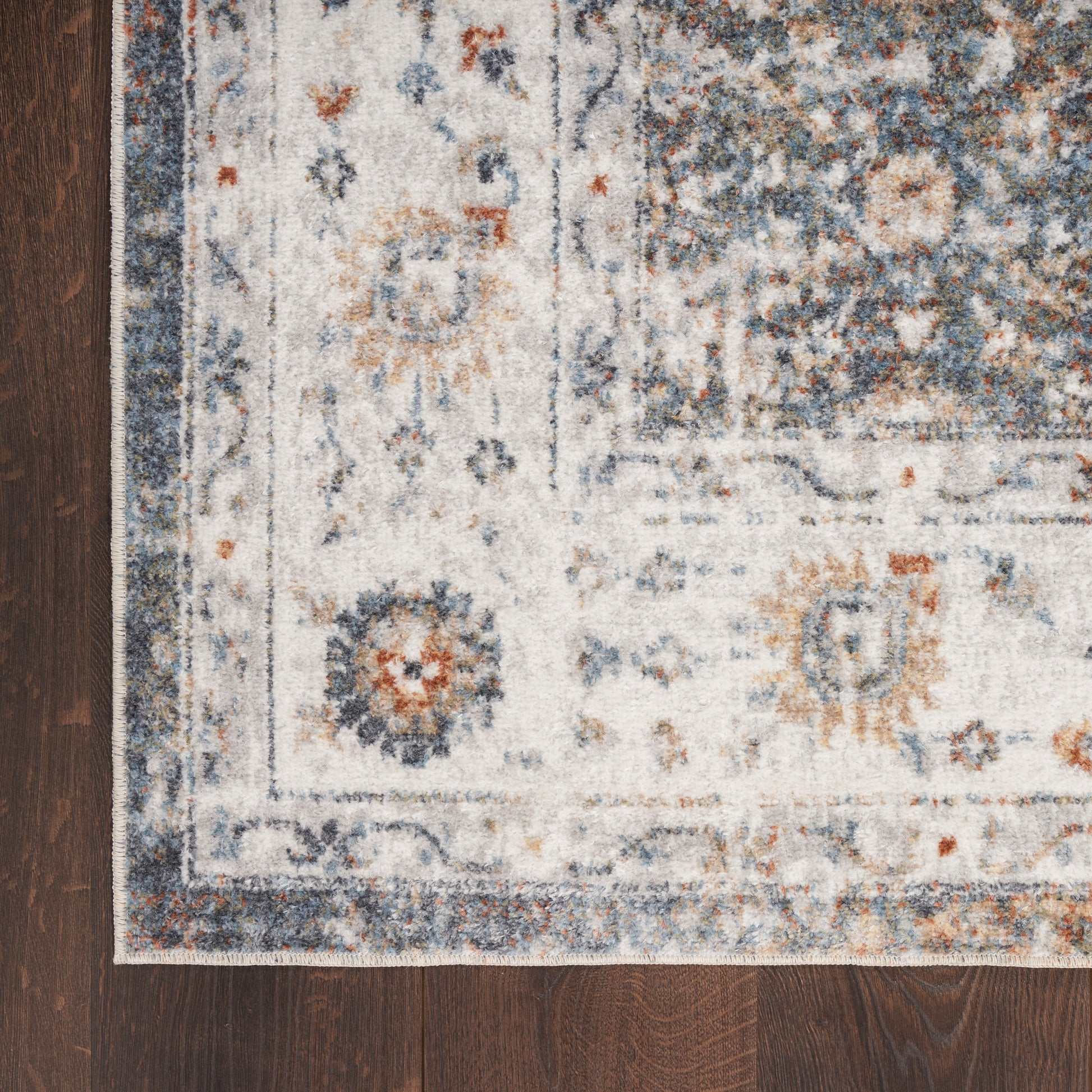 Ivory runner rug with blue floral motifs & decorative border on dark wooden floor.