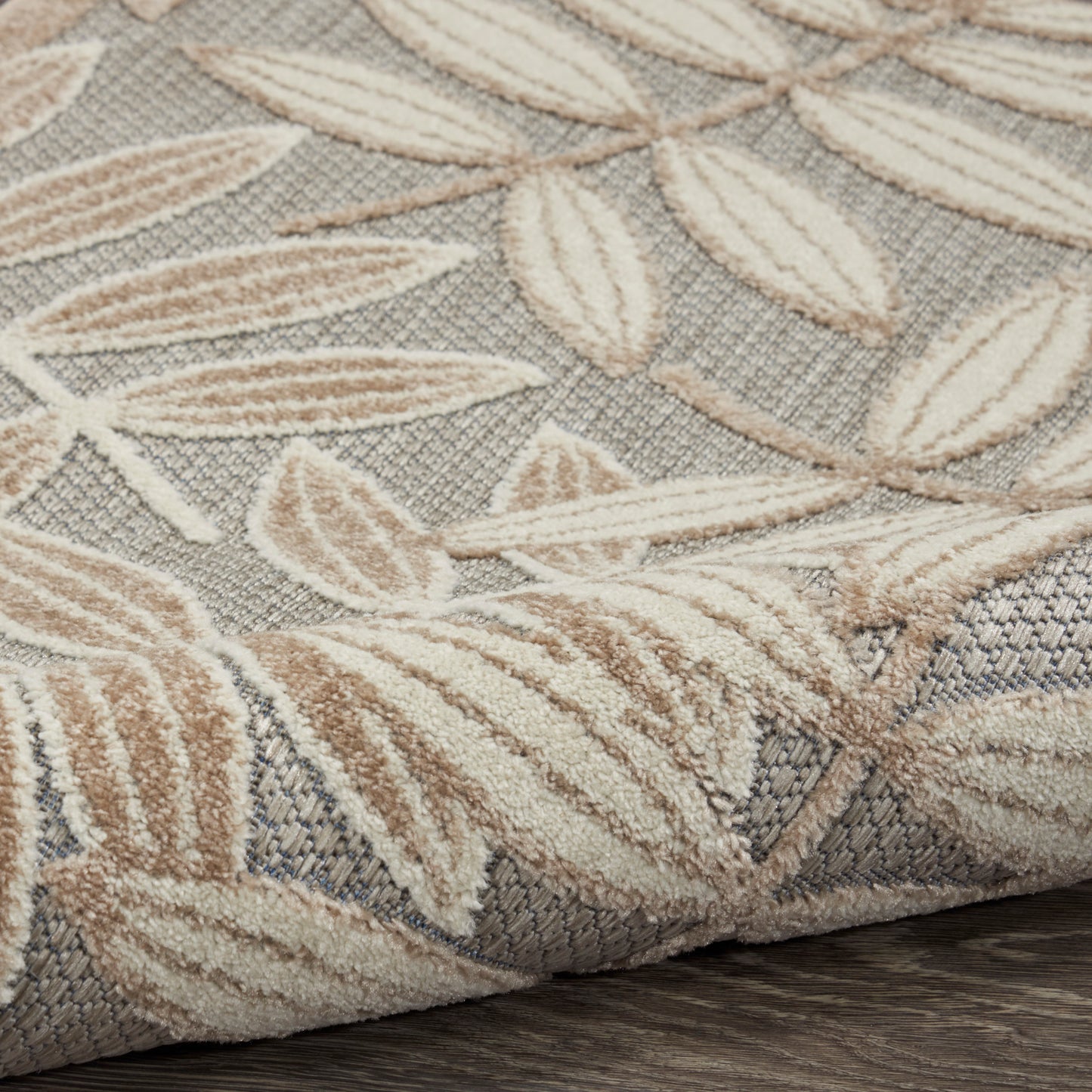 Leaf-pattern beige and cream rug with gray woven backdrop; tufted texture and rolled edge.