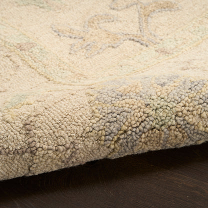 Close-up of beige rug edge with dense tufted pile on dark wood; subtle pastel floral pattern in cream, greens, and blues.