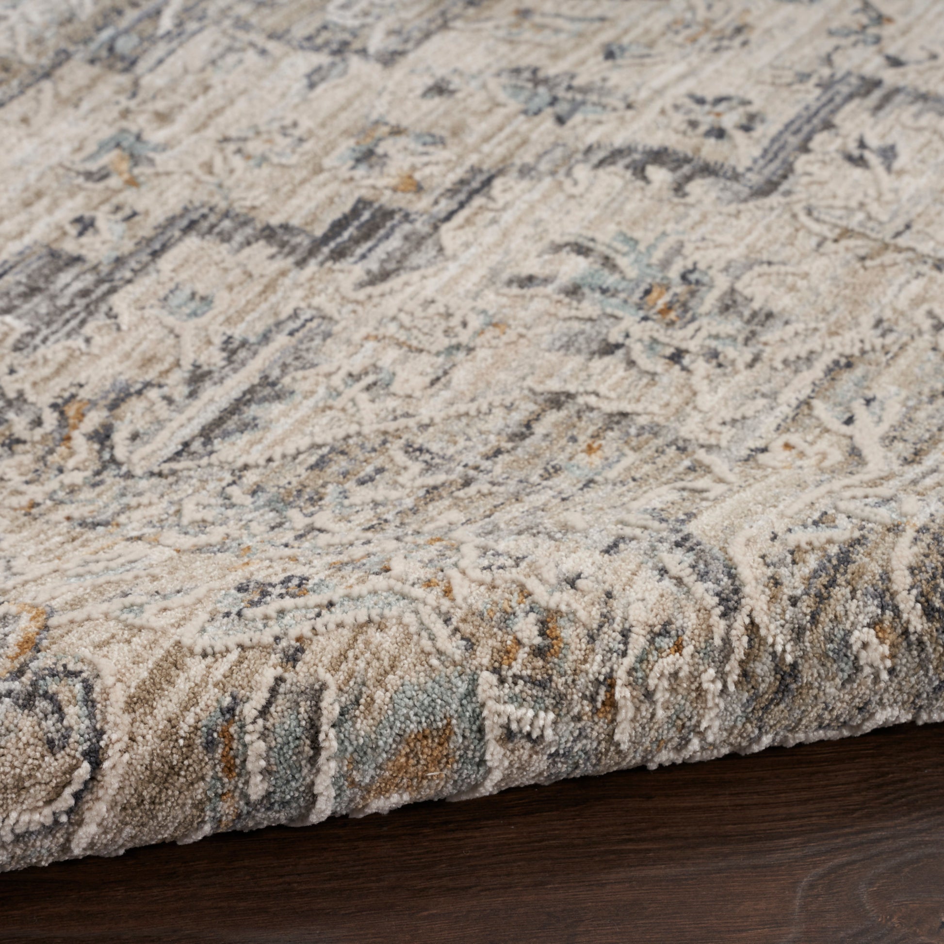 Soft beige, ivory & blue distressed oriental rug with gray accents; thick plush pile on dark wood floor.