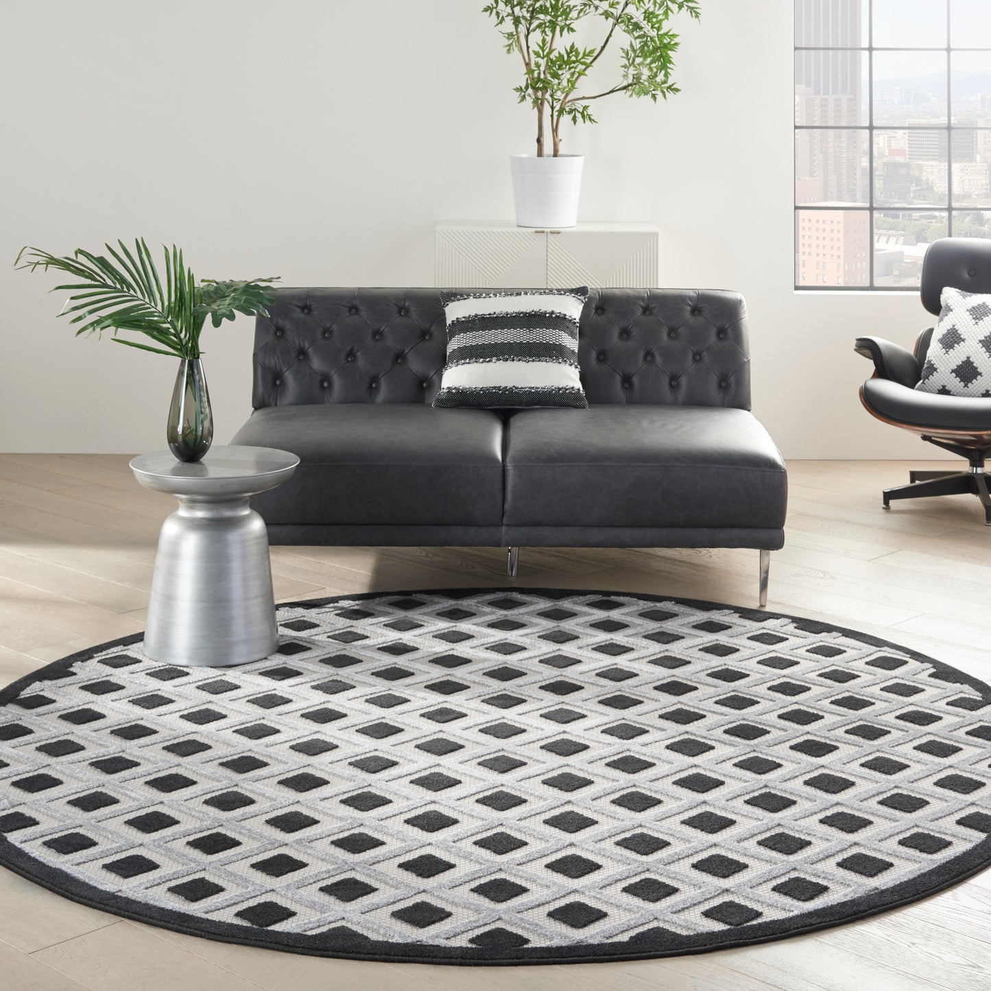 Round black-and-white geometric rug under a modern black tufted sofa; metal side table with a plant.