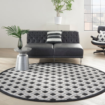 Round black-and-white geometric rug under a modern black tufted sofa; metal side table with a plant.