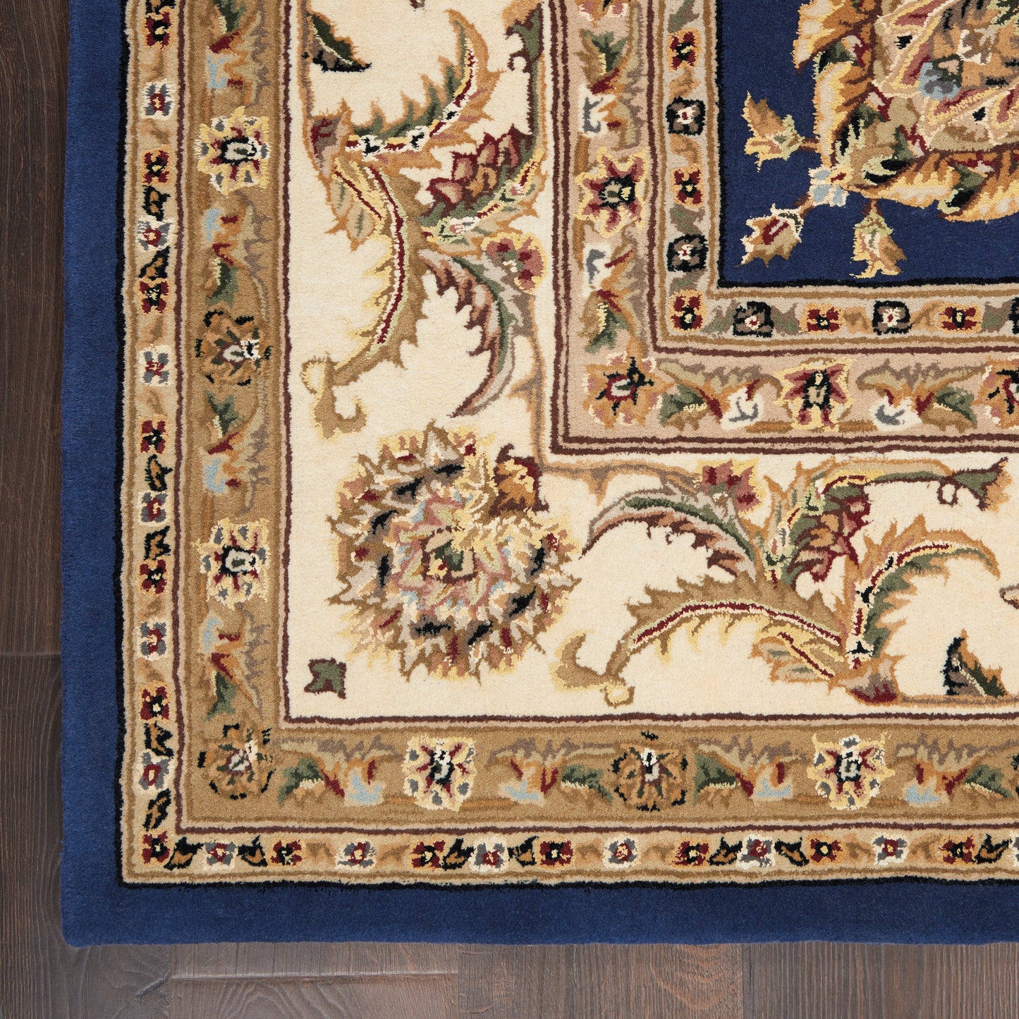 Corner view of an ornate Persian-style rug with cream field, blue border, and gold floral accents for living room decor.