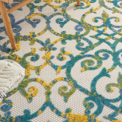 Colorful ornate rug with teal, blue, and mustard scrollwork on cream lattice; wooden chair legs and white fringe visible.