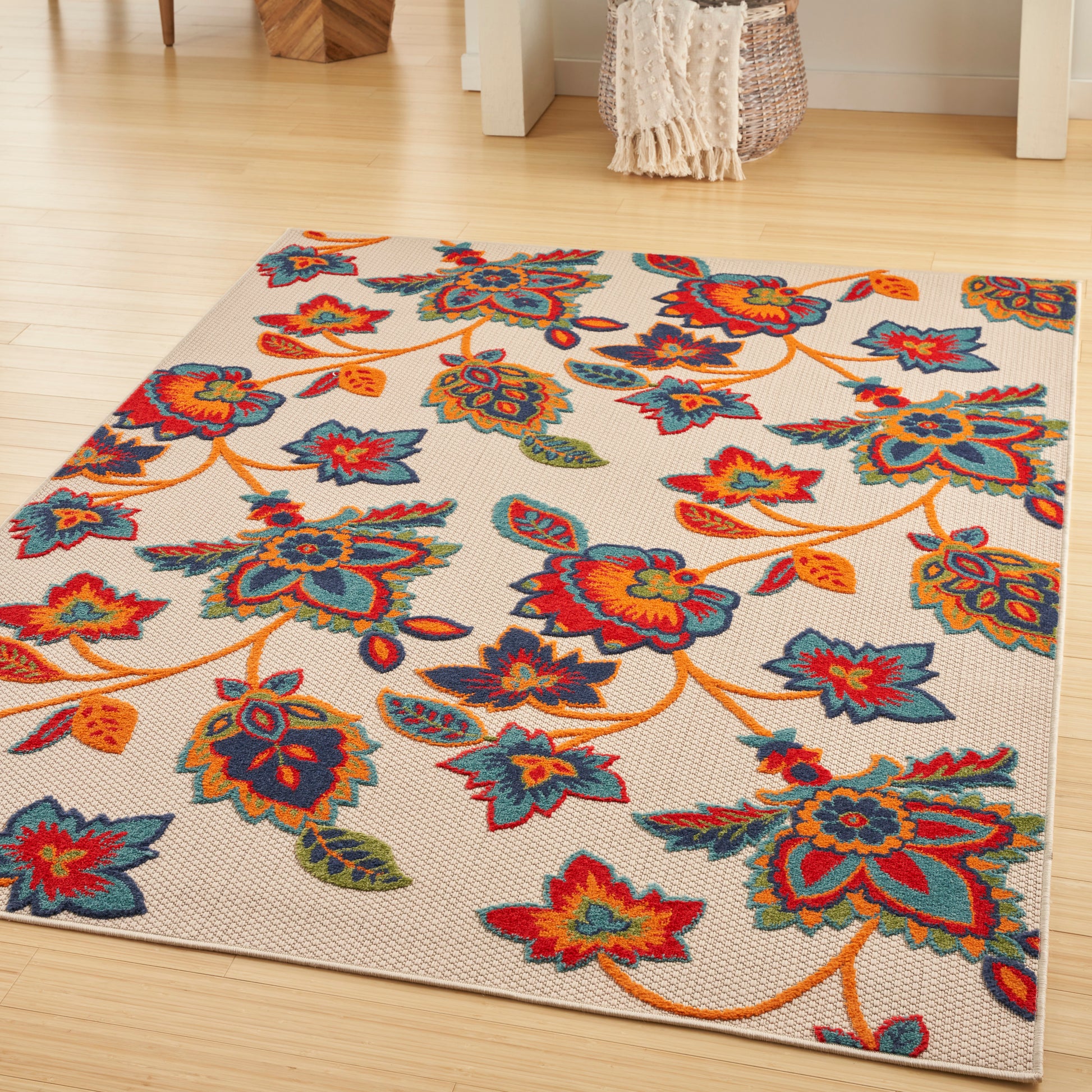 Bright floral area rug on light beige background with orange vines; red, blue, teal and yellow blossoms.