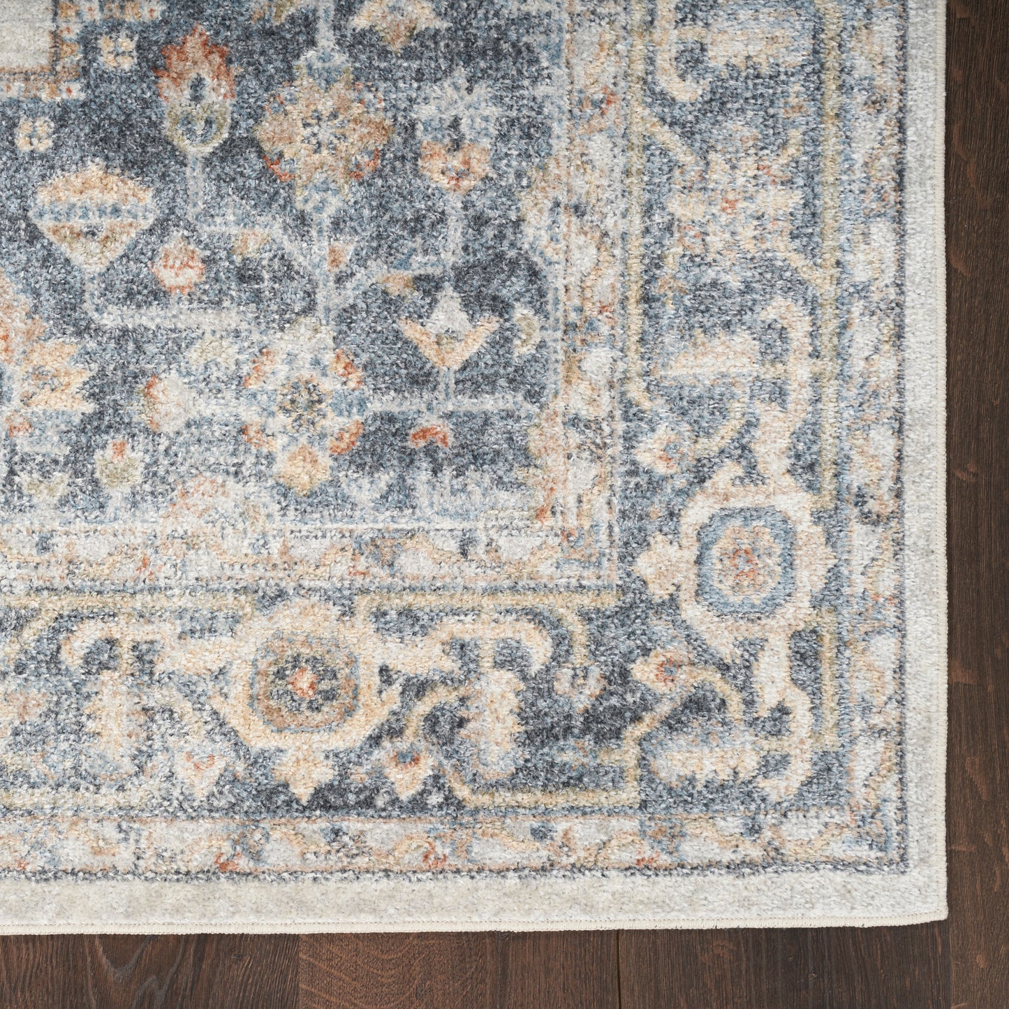 Blue Persian-inspired rug with ivory and peach motifs, distressed pattern, bordered edge, laid on dark wood floor.