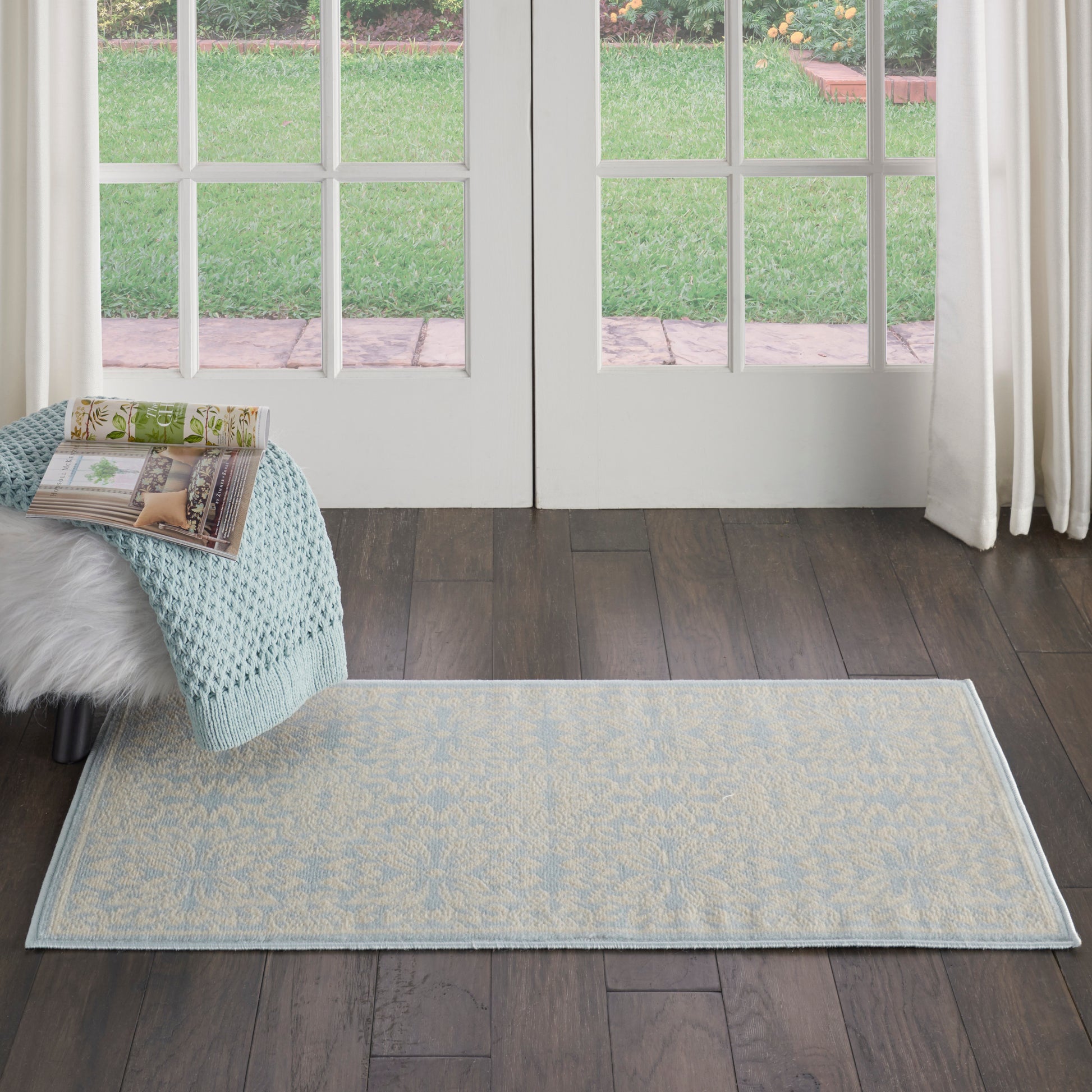 Rectangular pale blue woven rug with subtle cream damask pattern and light border on dark hardwood floor.