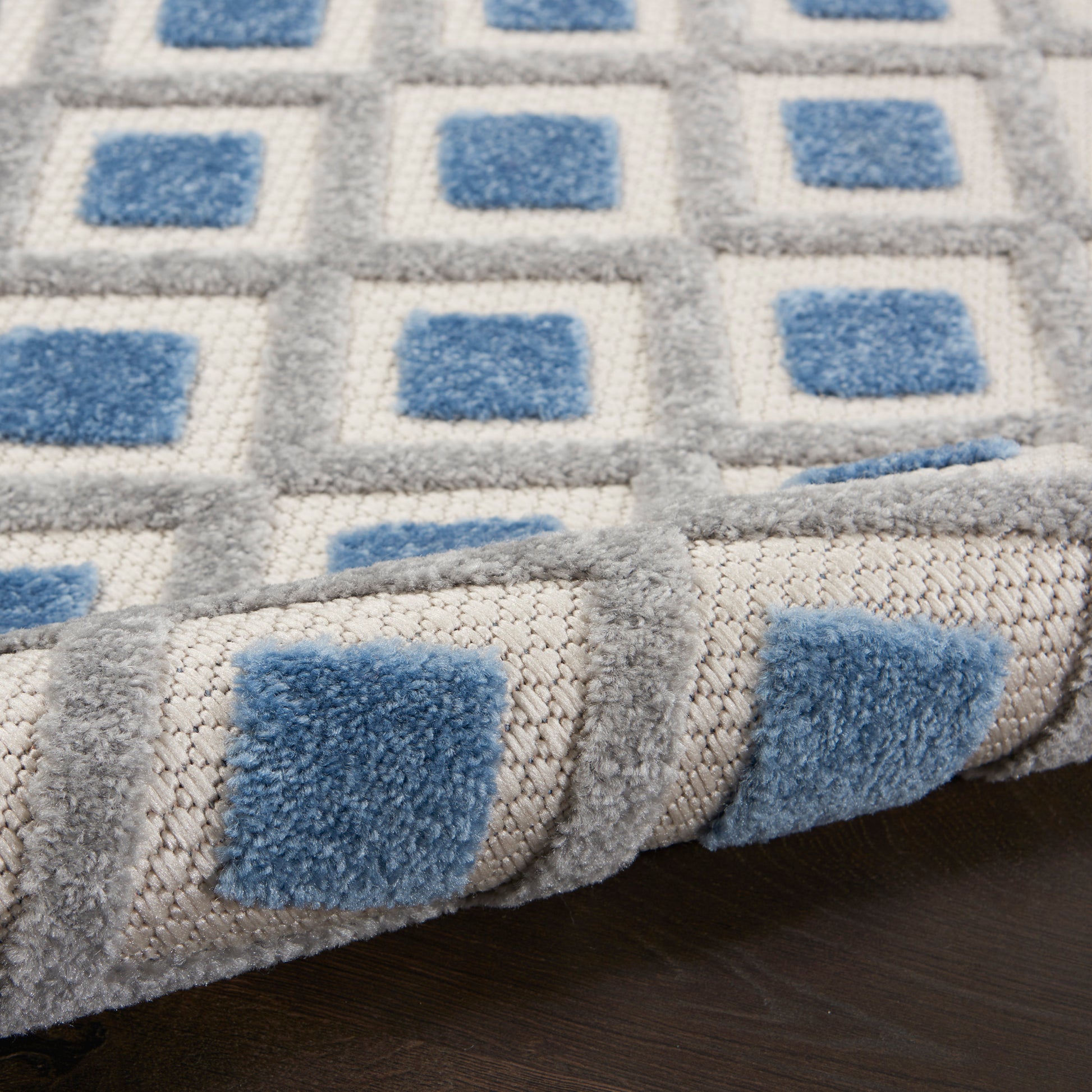 Soft gray rug with blue square motifs and plush pile; geometric pattern, close-up corner