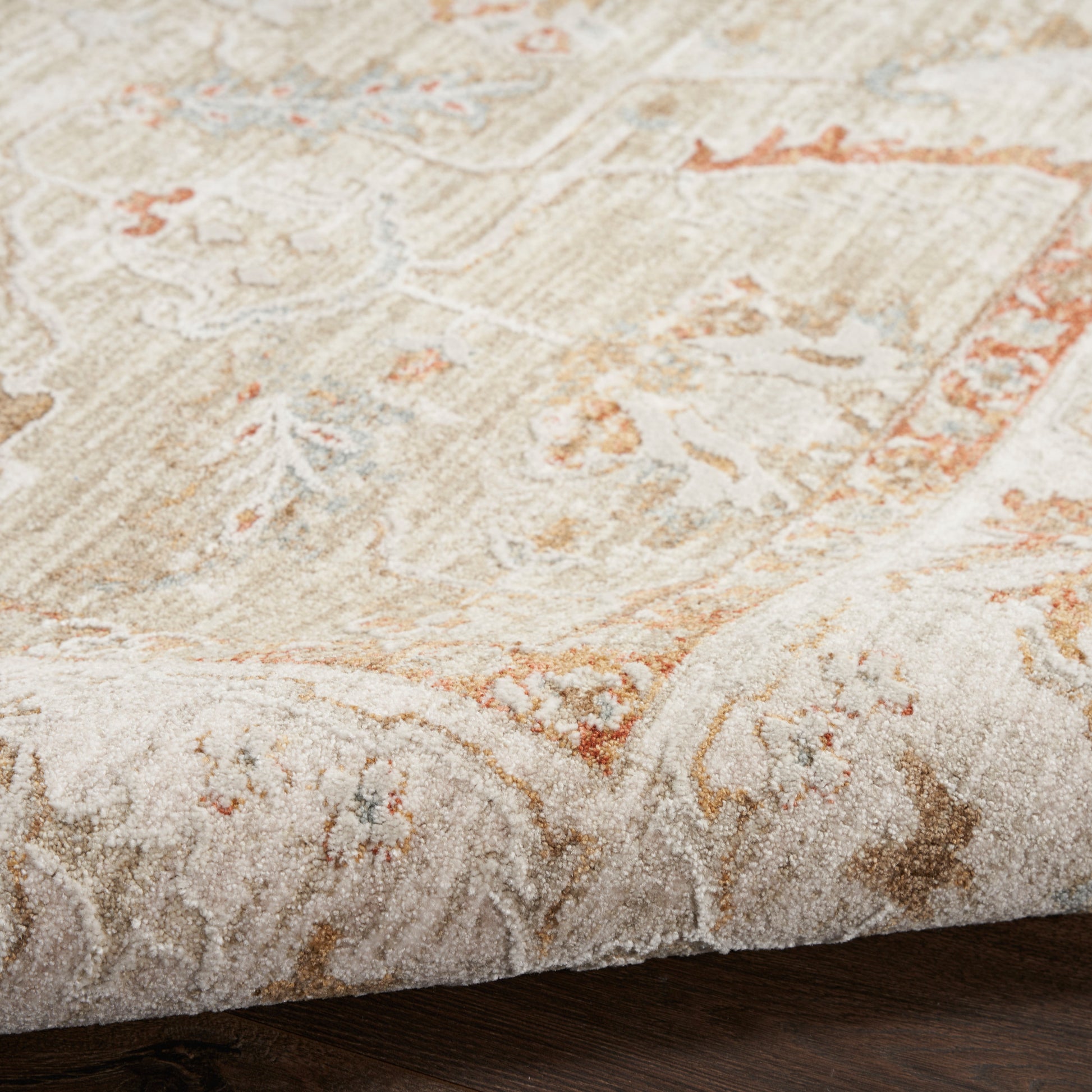 Rectangular, plush beige rug with cream floral pattern and orange accents on dark wood floor.