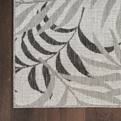 Rectangular woven runner rug with cream background and charcoal botanical leaf motif on a dark wood floor.