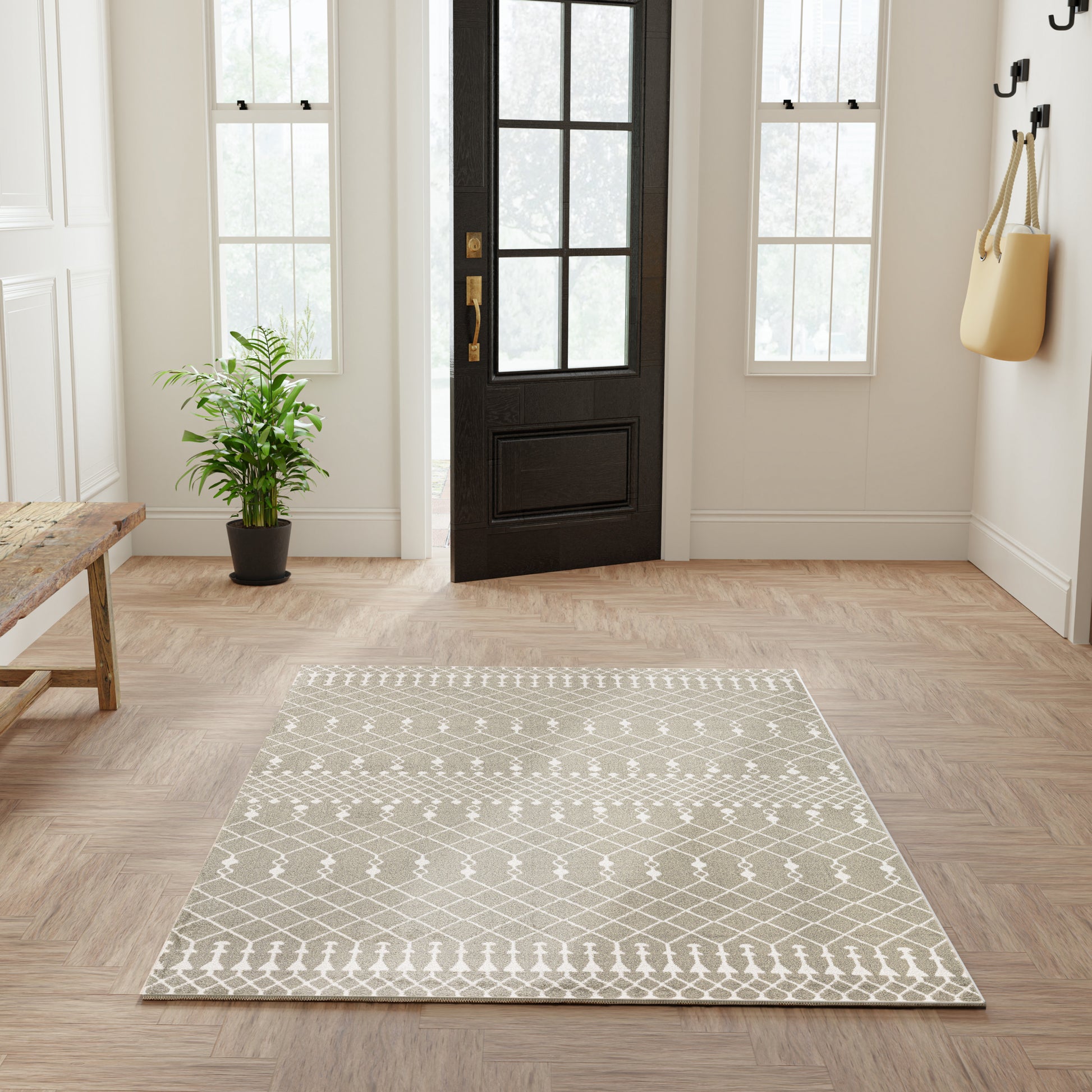 Entryway with black paneled door, beige lattice rug, light wood floor, potted plant, bench, and wall hooks with a bag.