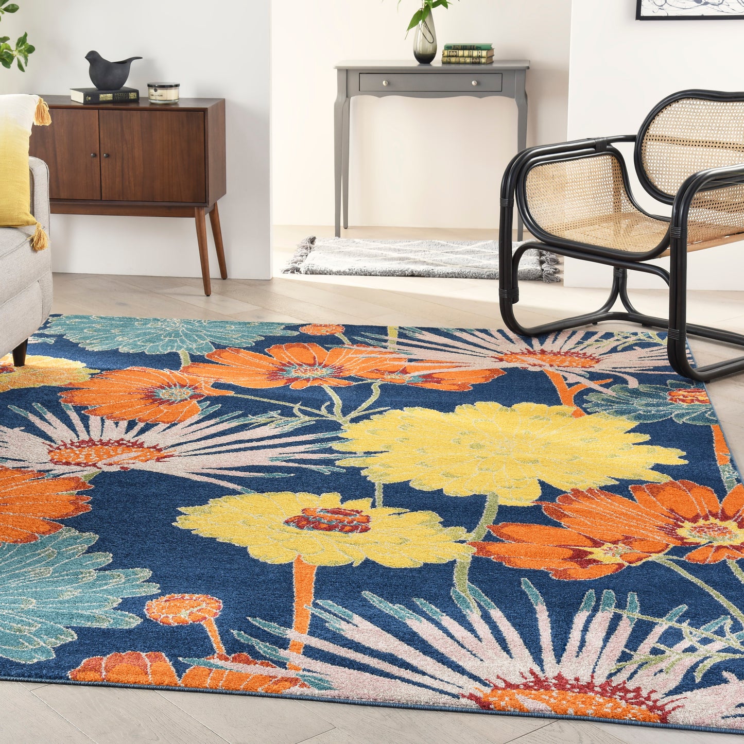 Vibrant floral area rug with navy background and orange-yellow blooms; woven texture in a living room with cane chairs.