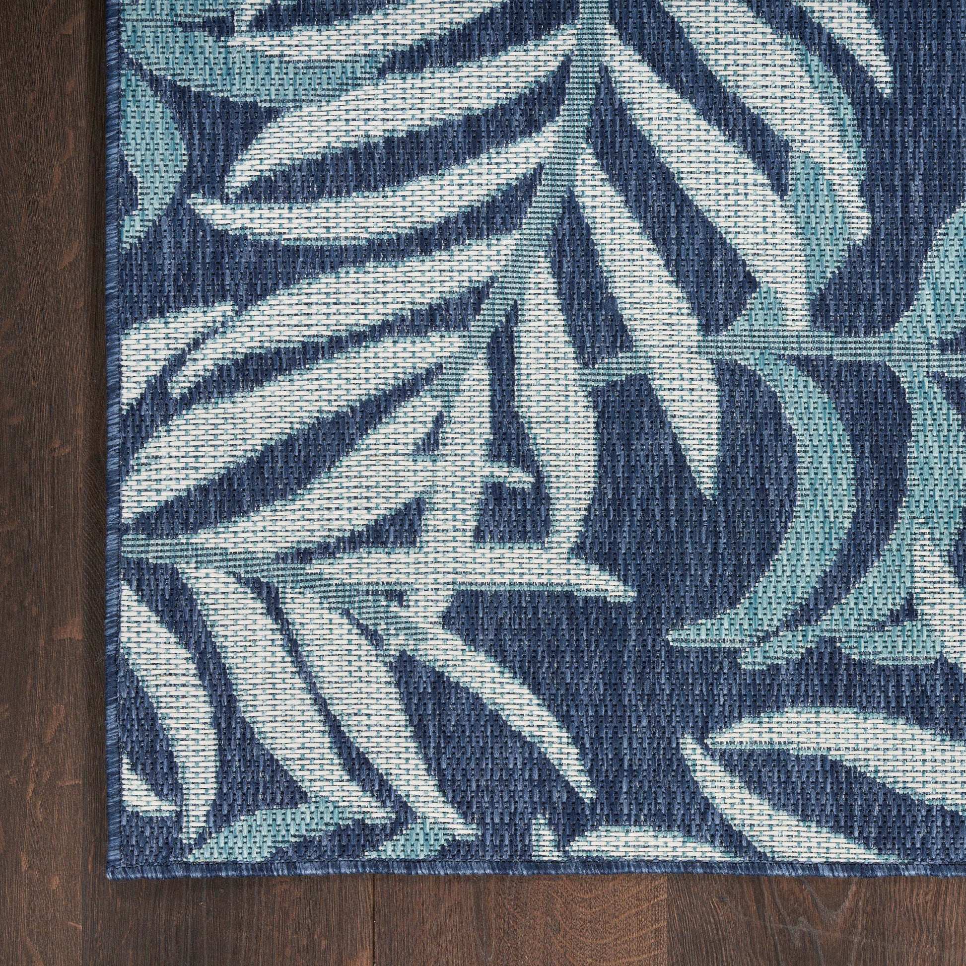 Navy woven rug with teal and ivory palm-leaf pattern; rectangular, coastal style.