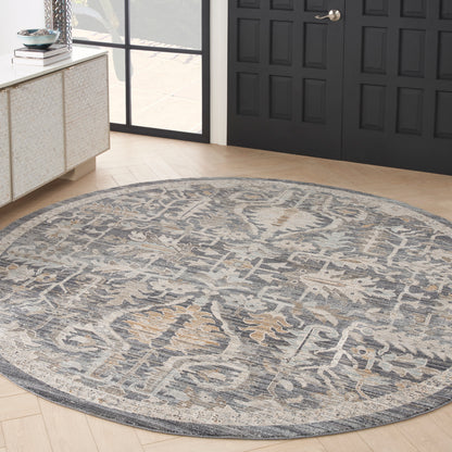 Round blue-gray woven rug with beige pattern, traditional oriental style, on light wood floor beside dark paneled doors.