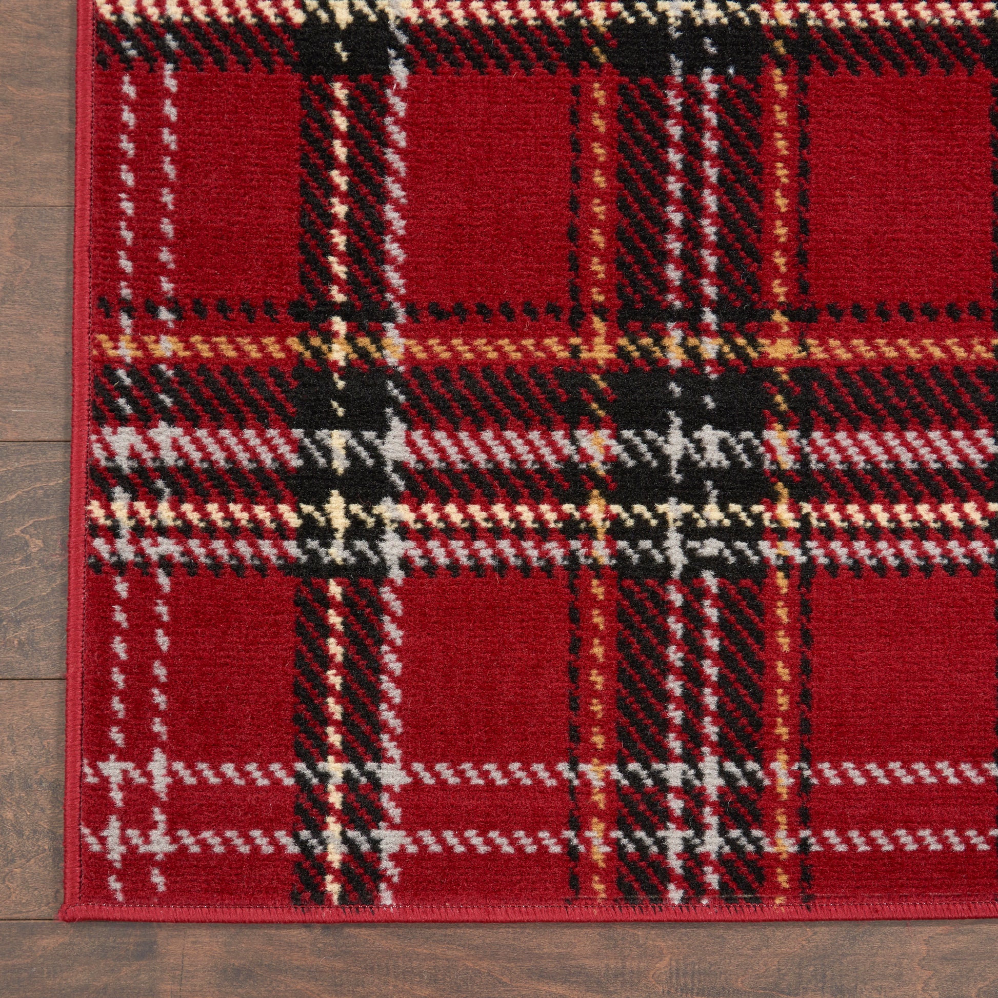 Red plaid woven rectangular rug with black, white & tan stripes on wood floor.