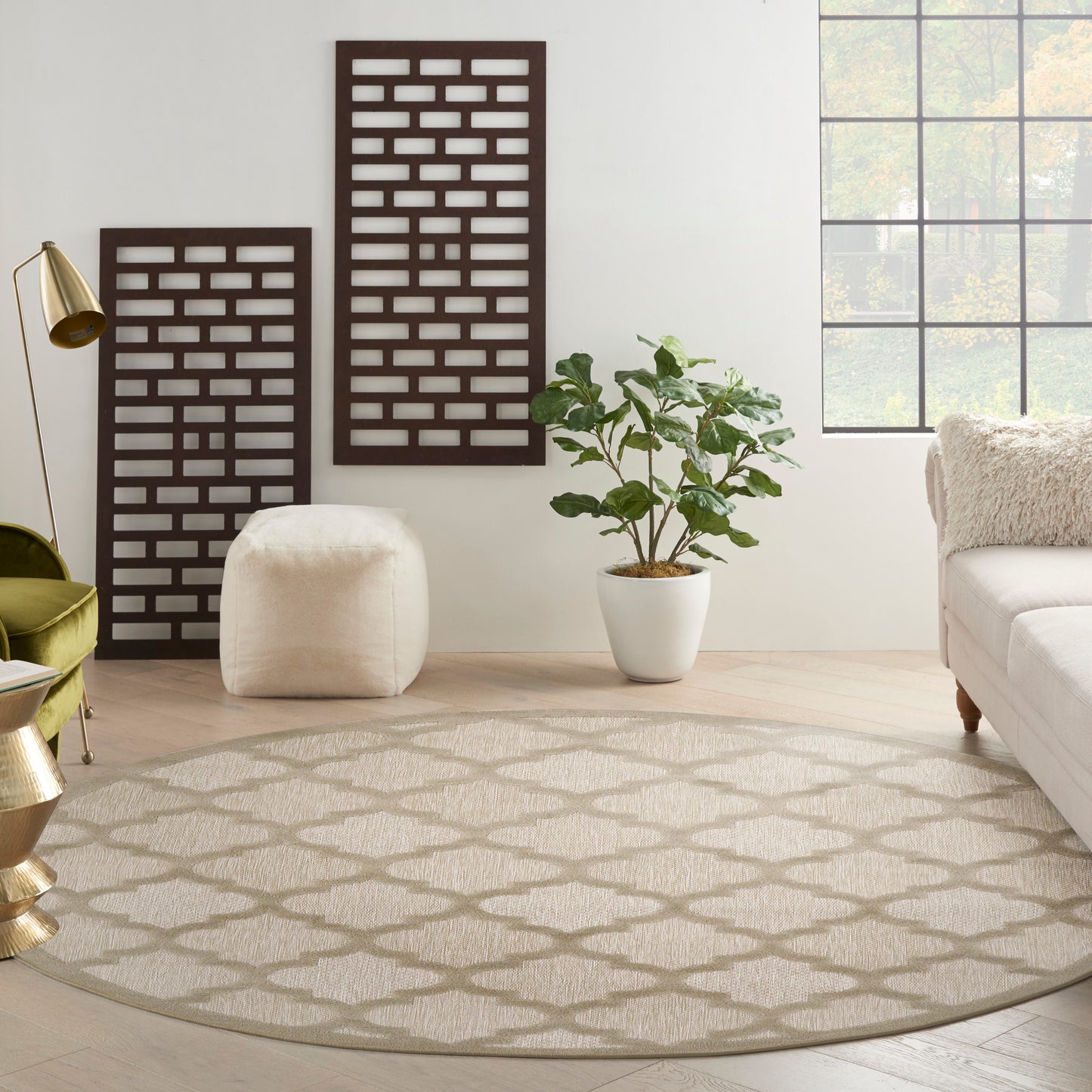 Round beige patterned rug in a bright living room with dark lattice panels, white pouf, potted plant, and sofa.
