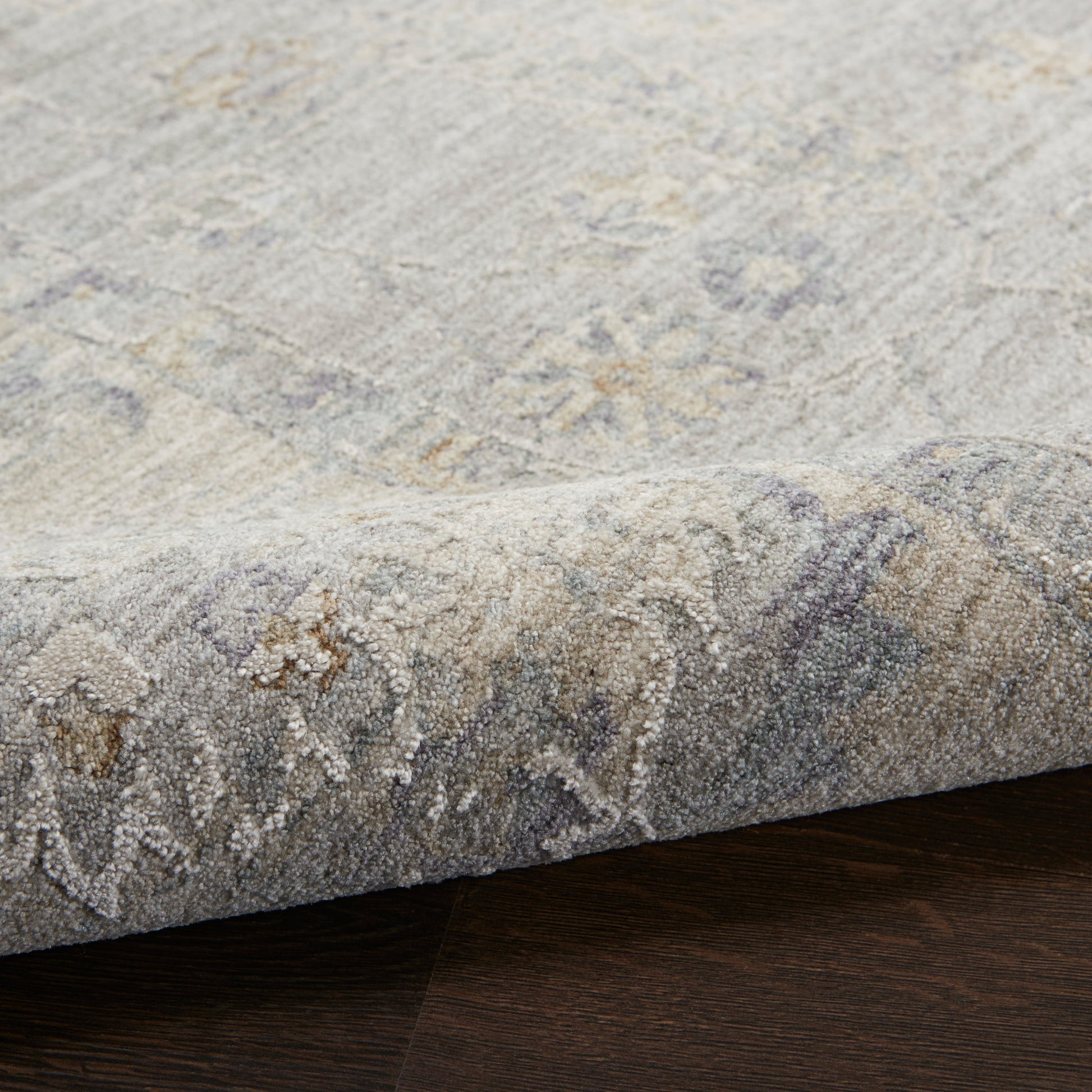 Soft gray patterned rug with beige and blue accents, woven texture, edge folded on dark wood floor