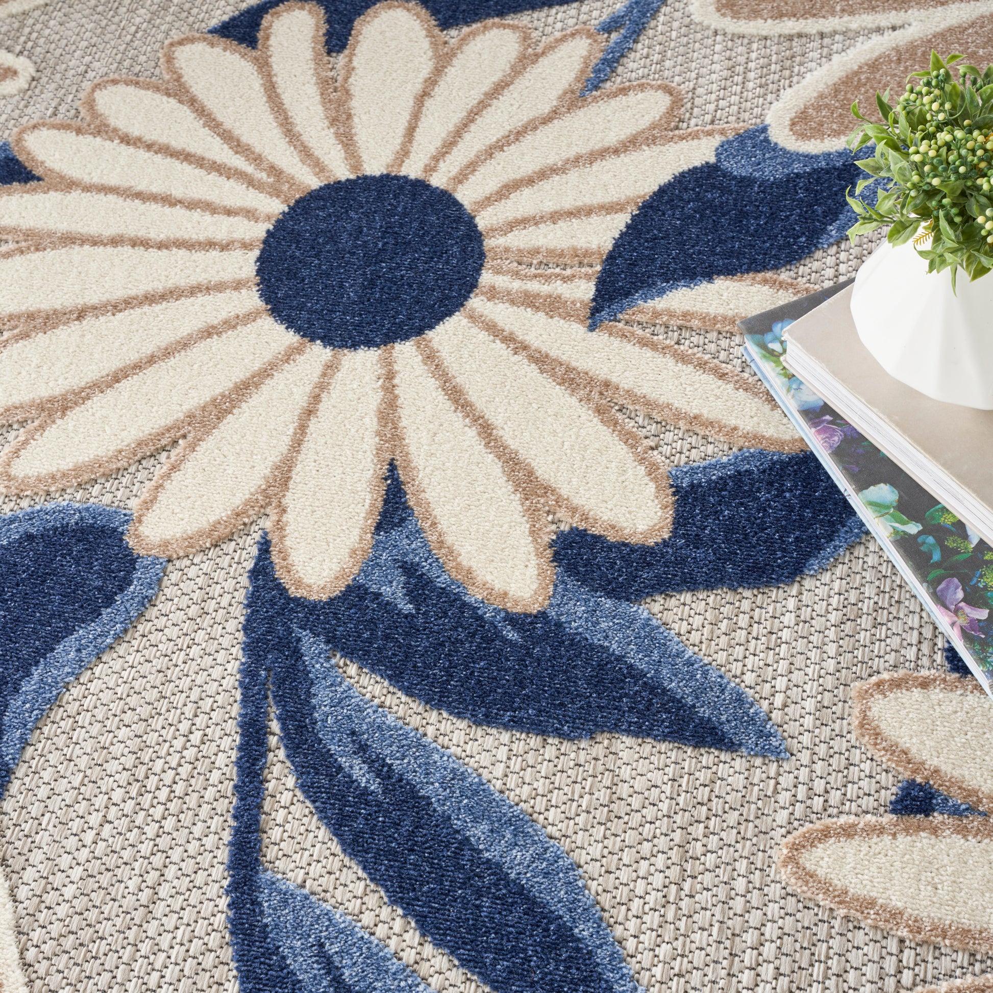 Large floral rug featuring a cream daisy with navy center and blue leaves on a woven beige background.