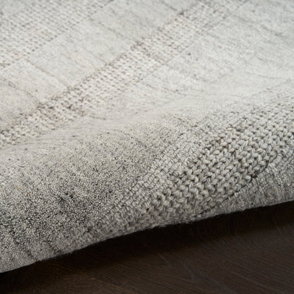 Light gray textured woven area rug with subtle plaid pattern and bound edge on dark wood floor.