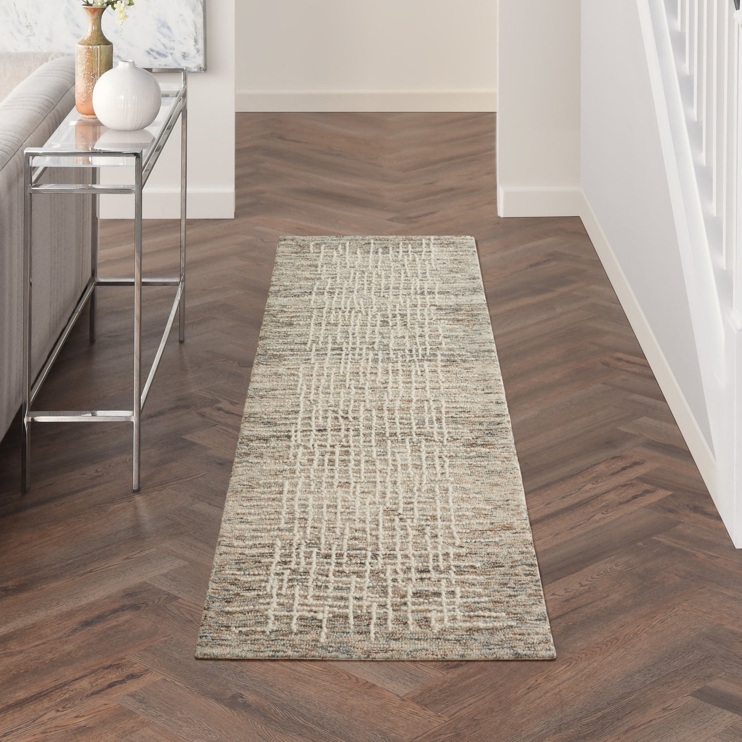 Long hallway runner rug in neutral beige-taupe tones with a geometric grid pattern on dark herringbone flooring.