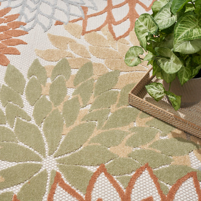 Leaf-pattern outdoor area rug in green, beige, & orange with a potted pothos on a woven tray.