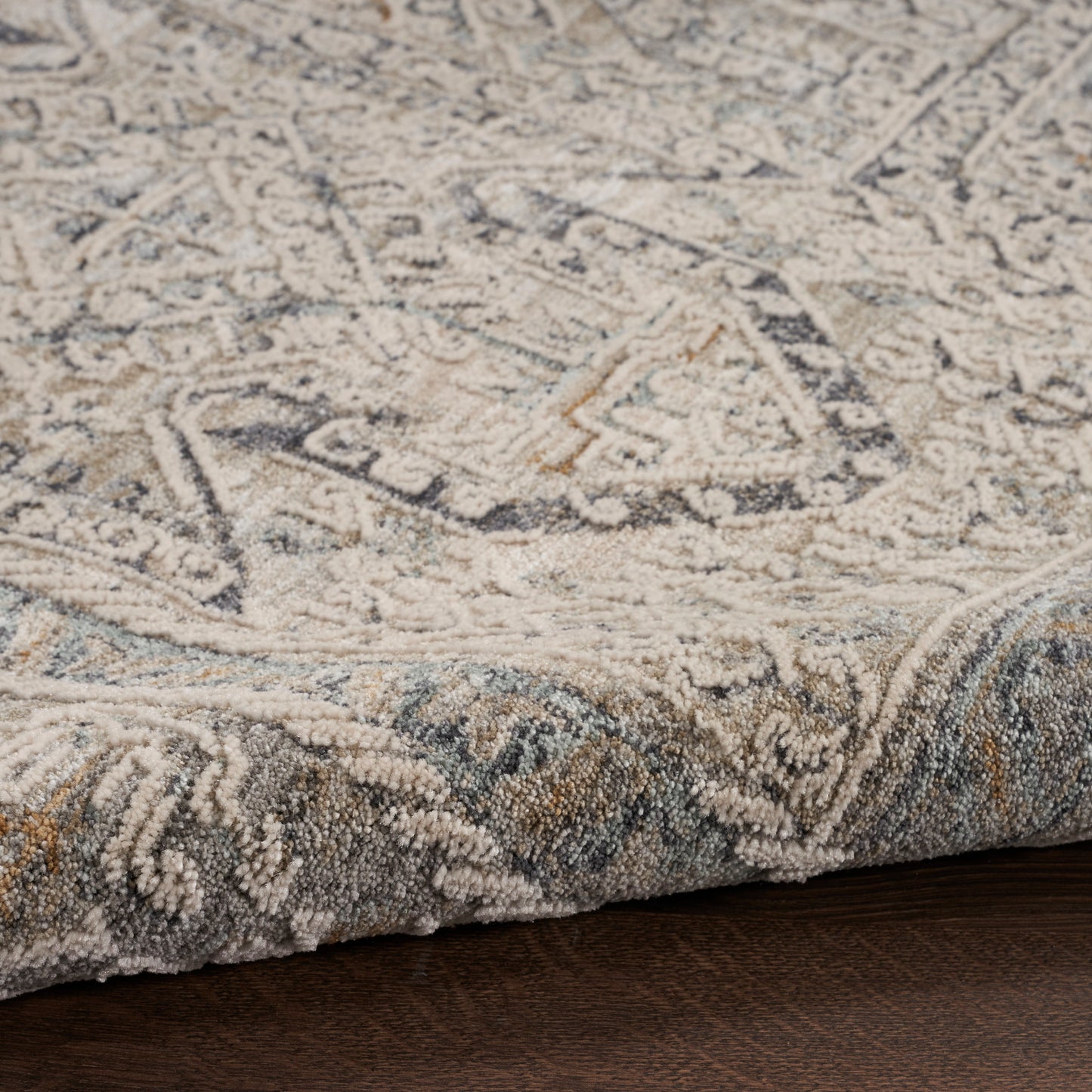 Neutral-toned oriental area rug with ivory, gray and blue motifs, textured pile on dark wood floor.