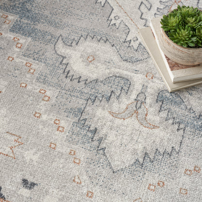 Soft gray-blue rug with abstract geometric pattern in blue and orange, shown with a succulent on books.