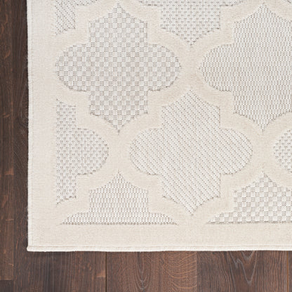 Cream flatwoven rug with large interlocking quatrefoil lattice pattern on dark wood floor.