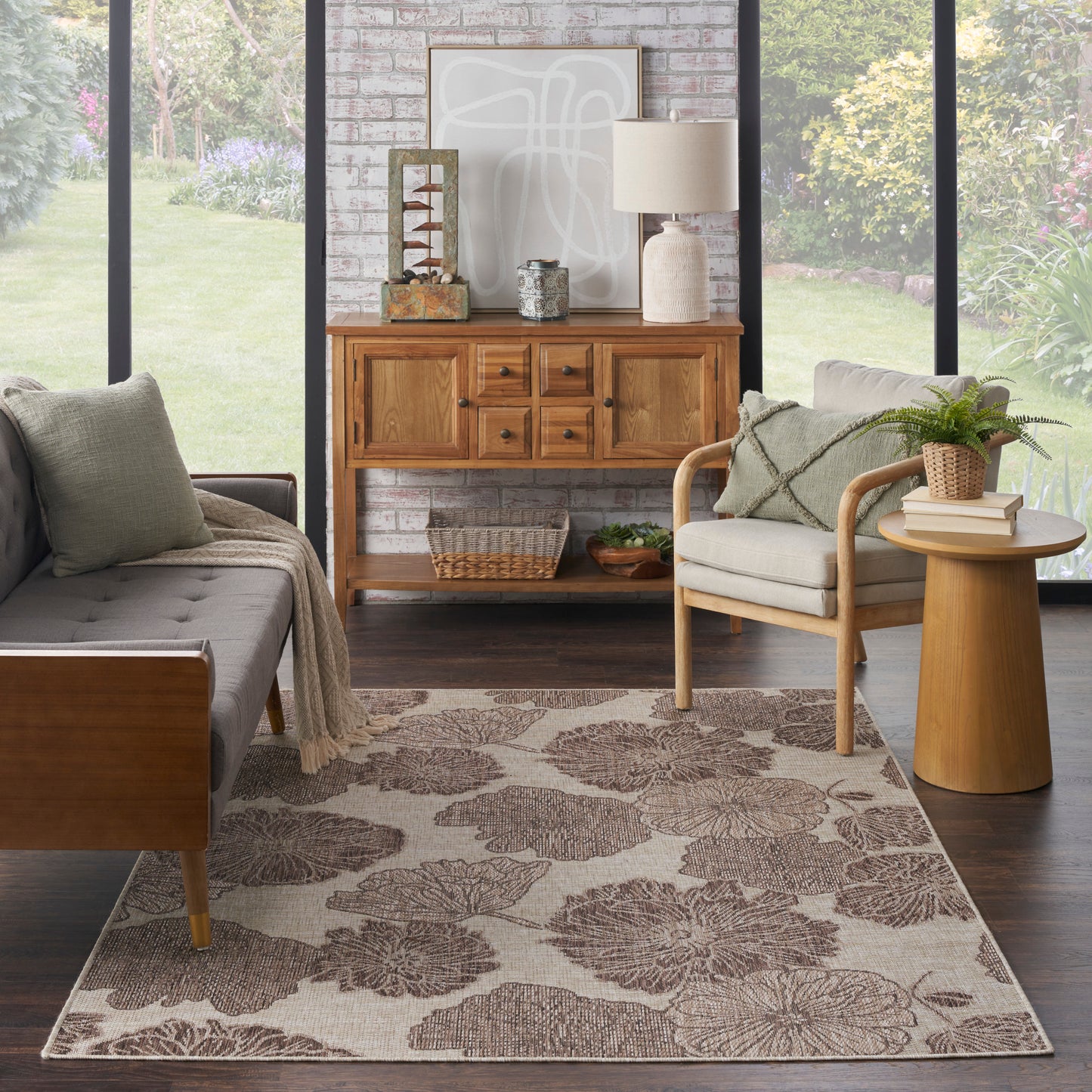 Cozy living room with mid-century wood furniture, gray sofa, beige armchair, tropical rug, brick accent wall, wooden sideboard.