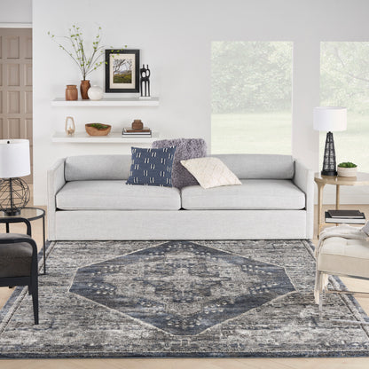 Light gray fabric sofa with navy and cream cushions in a bright modern living room with a blue-gray patterned rug.