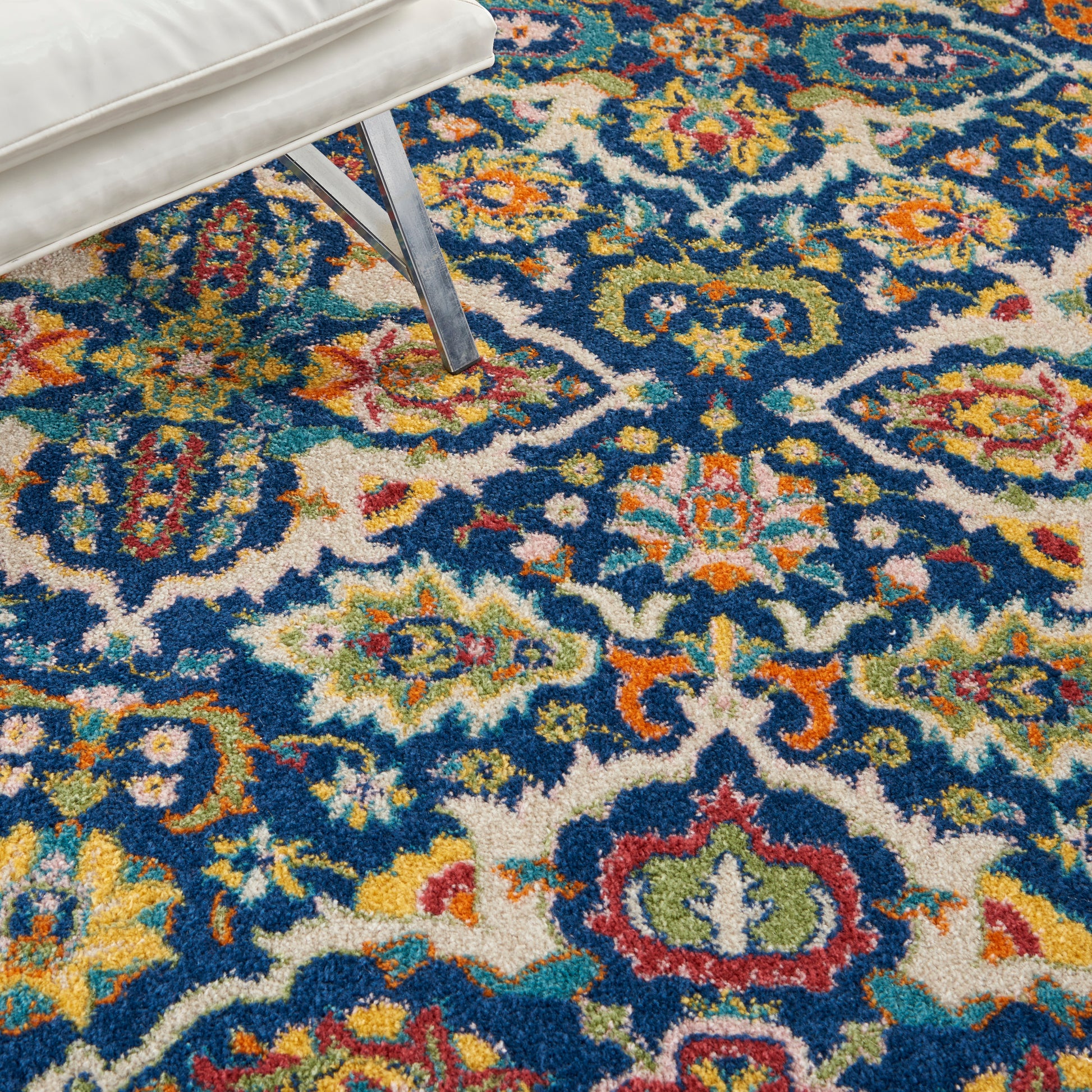 Colorful Persian-style area rug with blue field and bright floral motifs; white upholstered seating with metal legs nearby.