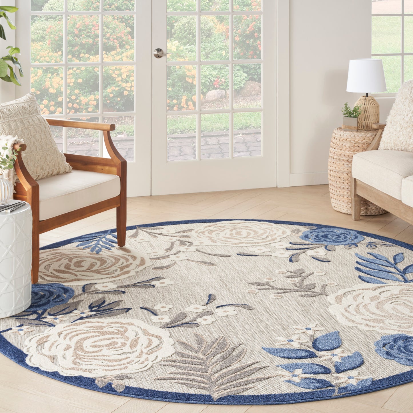 Circular beige rug with blue floral pattern (8' round) in a bright living room; wood chair, wicker side table, cream sofa.