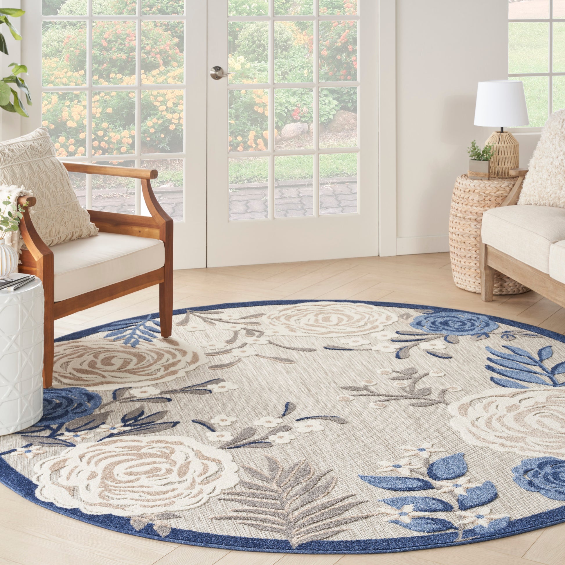 Circular beige rug with blue floral pattern (8' round) in a bright living room; wood chair, wicker side table, cream sofa.