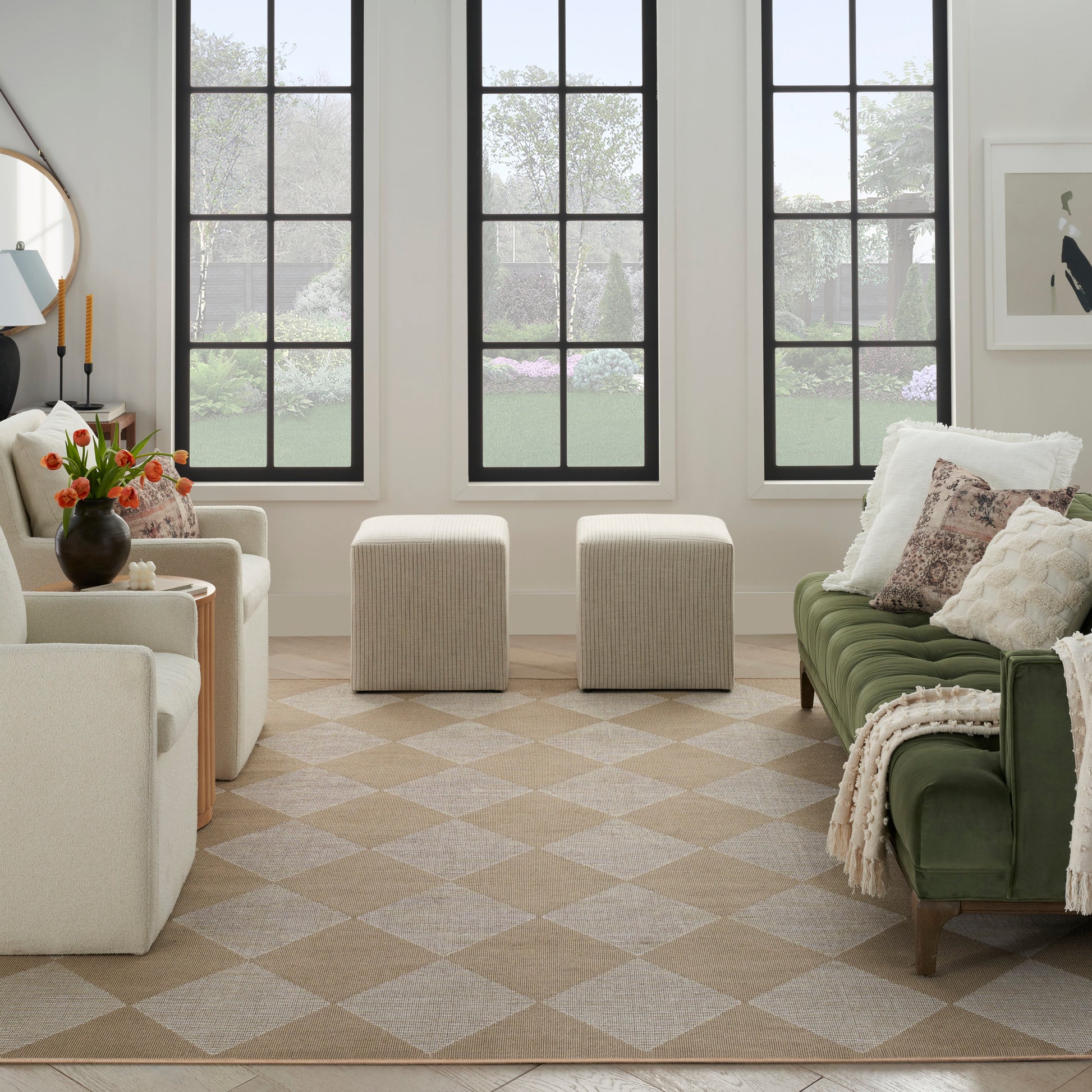 Neutral-toned living room with green velvet sofa, beige armchairs, cream ottomans, diamond rug, and vase of orange flowers.