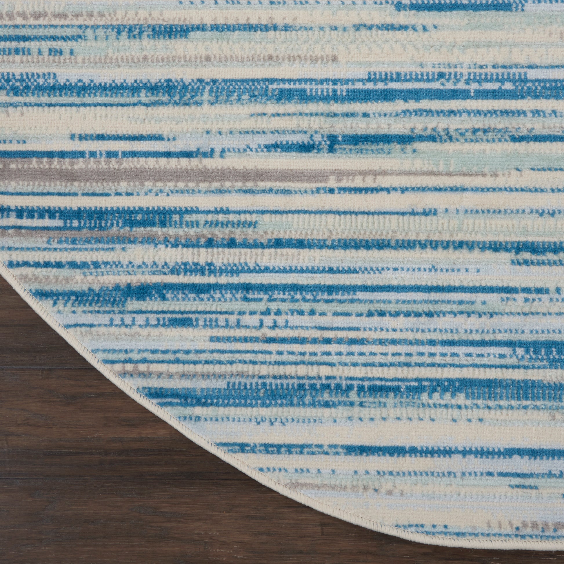 Blue and white striped round area rug on dark wood floor; woven textile with horizontal brushstroke pattern