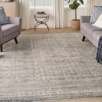 Geometric gray area rug in a living room with two gray sofas, blue pillows, a round metal side table, and a potted plant.
