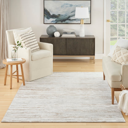 Neutral living room with cream armchairs, light gray rug, round wood side table, dark wood console, abstract art, white lamp.