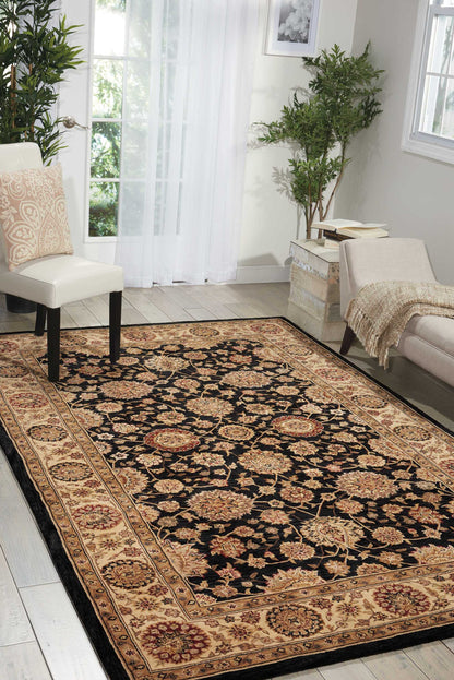 Living room with a large oriental rug: black center, gold floral border, cream chairs, sofa, plants, and sheer curtains.