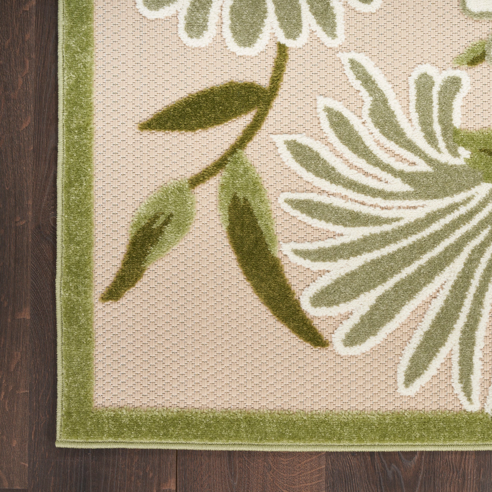 Beige woven area rug with olive-green border and large green botanical leaf pattern.